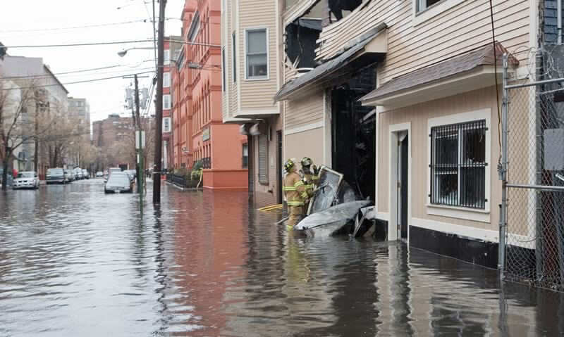 firefighters in flood next to damaged building